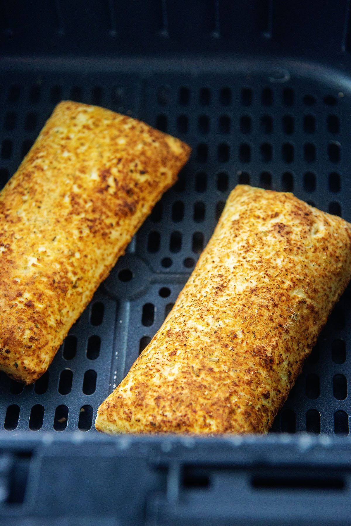 Close up of two hot pockets side by side in an air fryer basket.