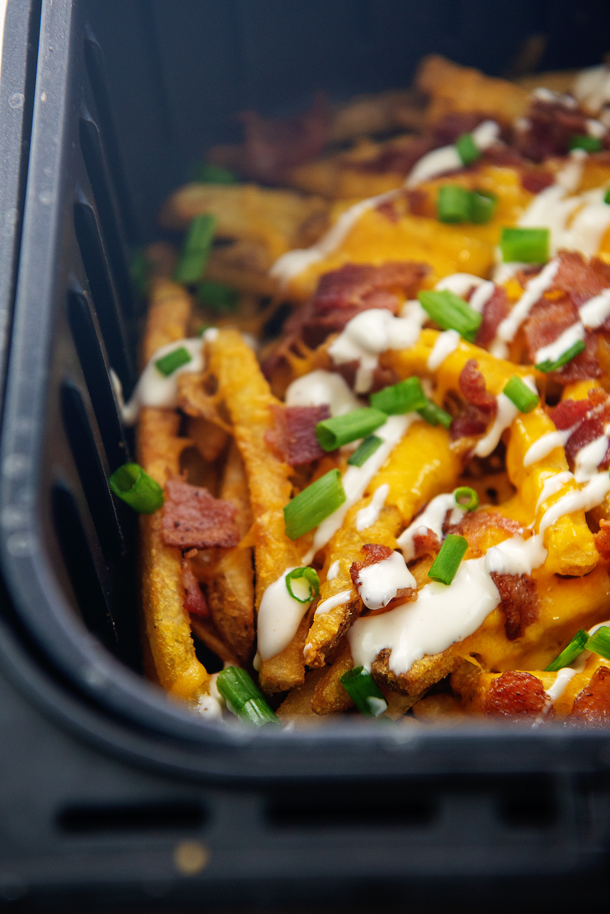 Close up picture of loaded fries in a black air fryer basket.