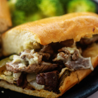 Philly steak sandwich with melted cheese on a black plate.
