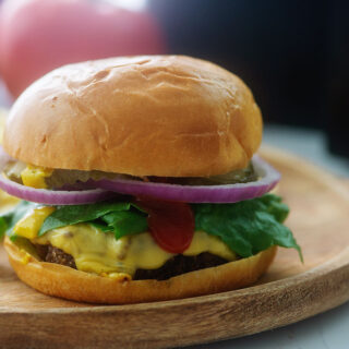 Side view of a cheeseburger on a wooden serving plate.