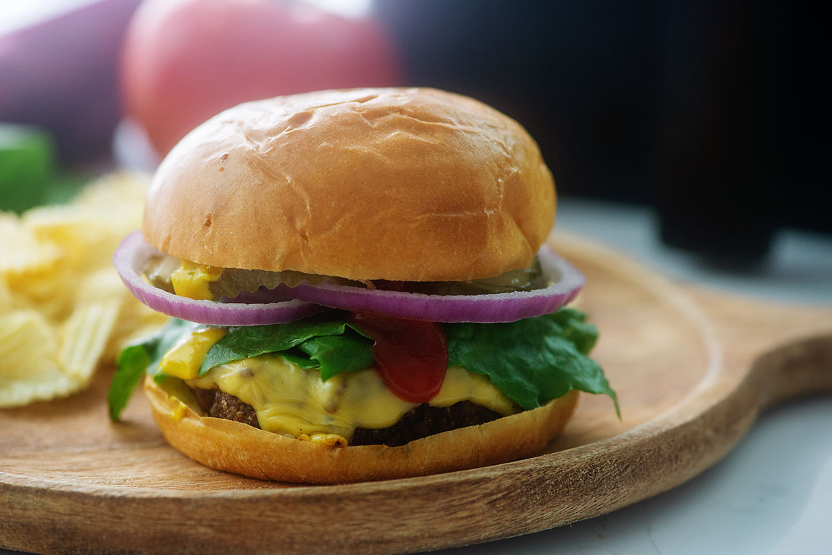 Side view of a cheeseburger on a wooden serving plate.
