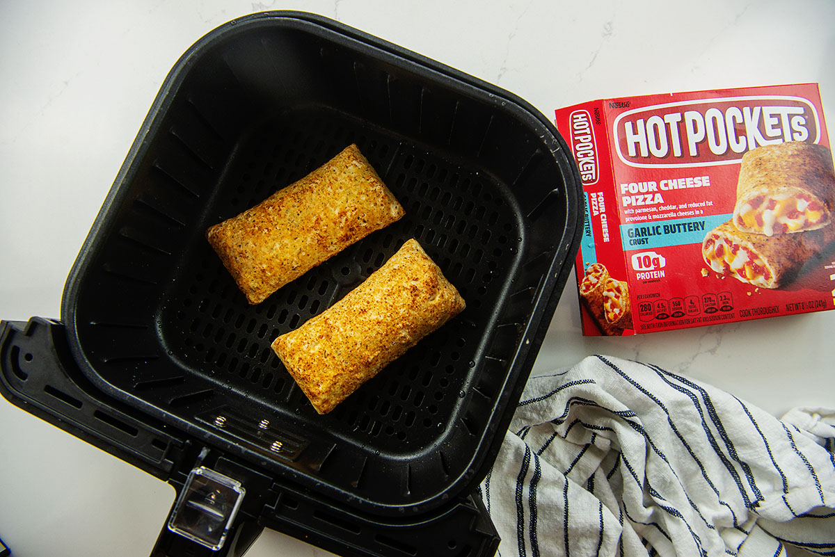 Pizza hot pockets in an air fryer basket next to the package they came in.
