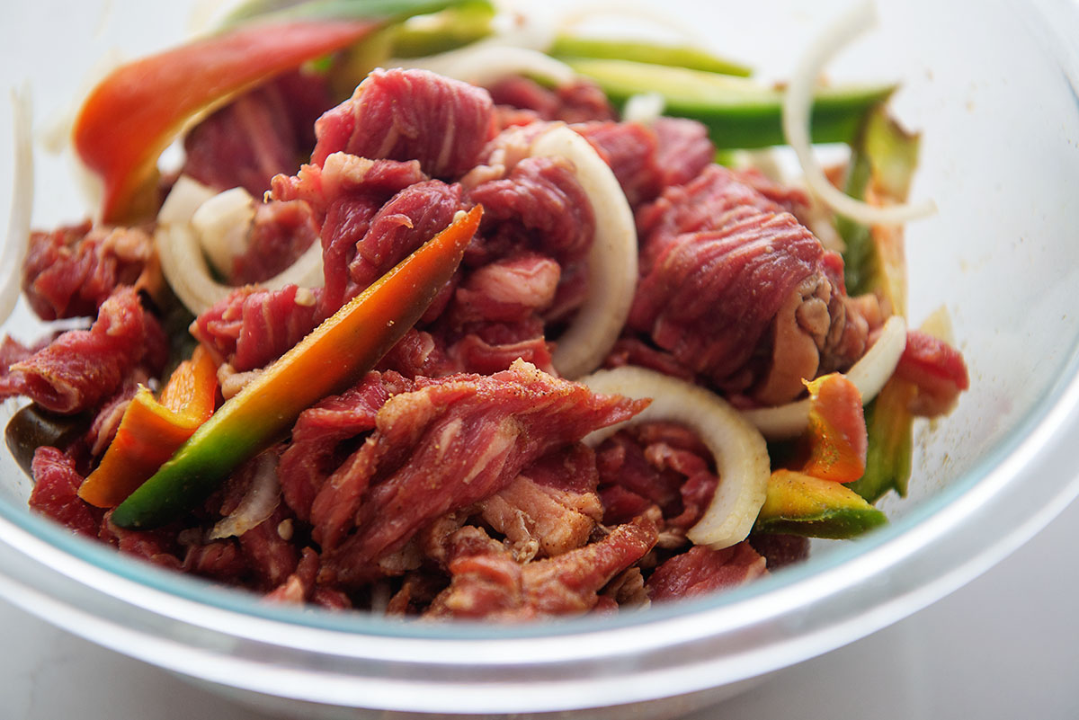 Raw beef and veggies in a clear glass bowl.