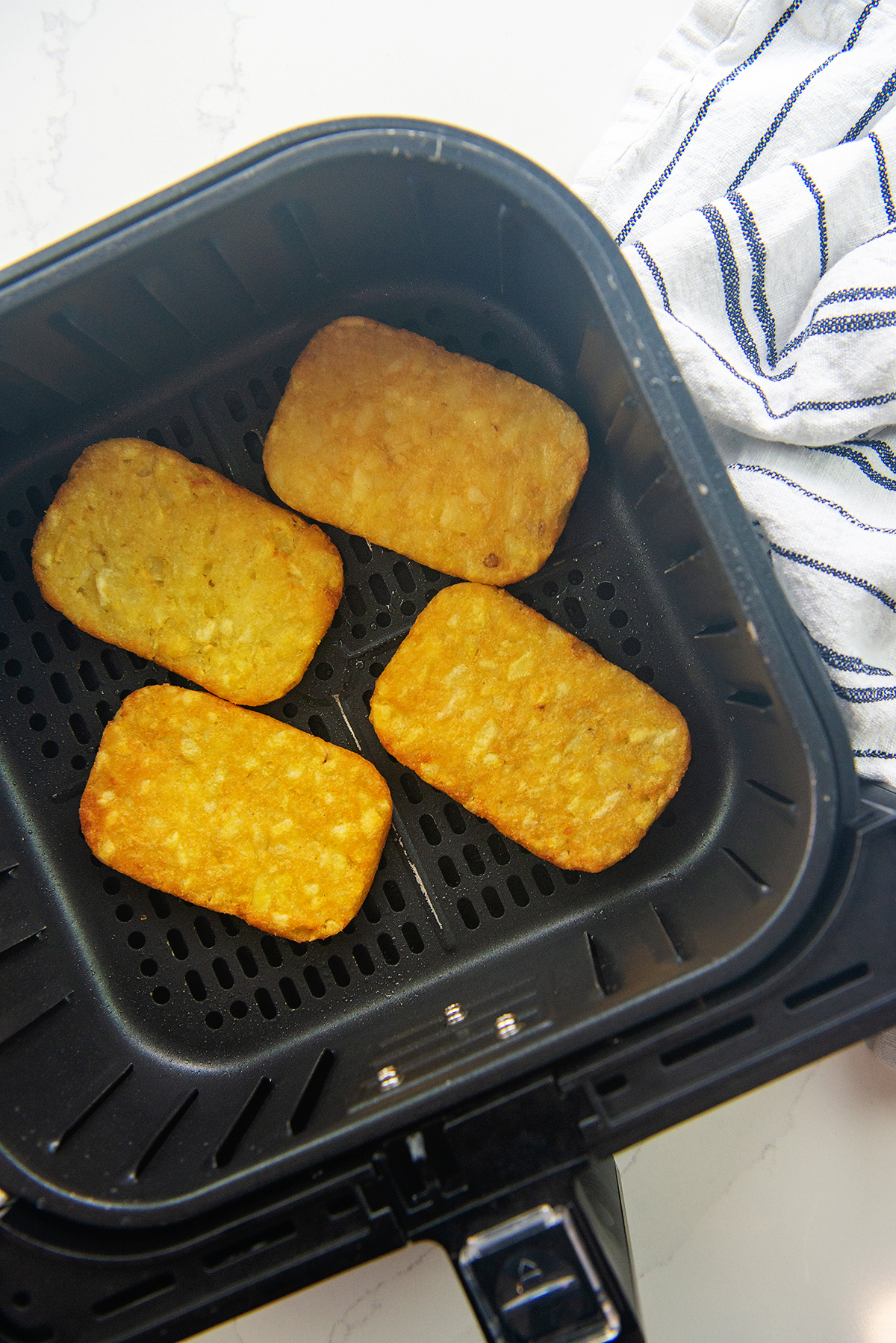 Four hashbrowns spread out in an air fryer basket.