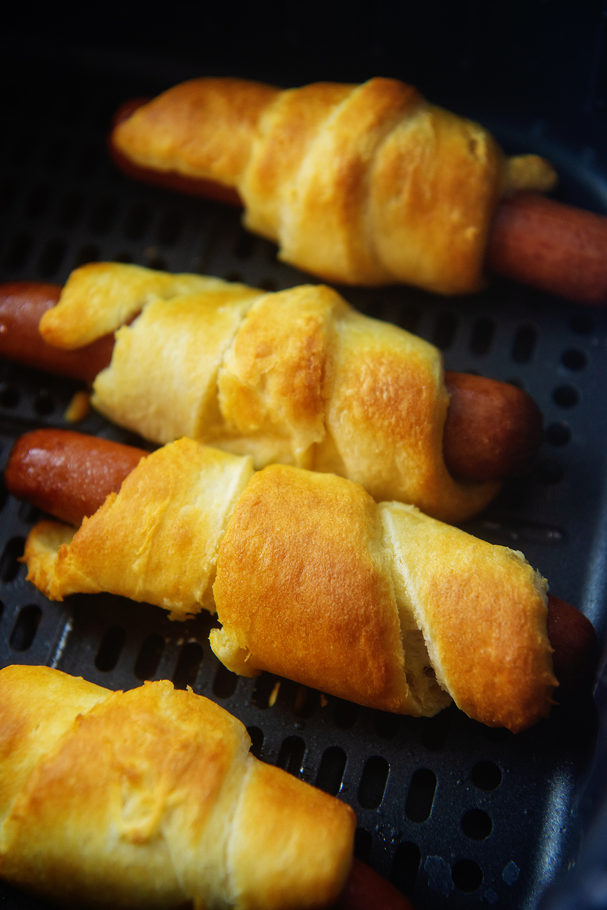 hot dogs wrapped in crescent dough in air fryer basket.