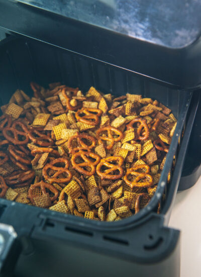 An air fryer basket with Chex mix being removed from the air fryer.