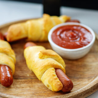 pigs in a blanket on wooden cutting board with ketchup.