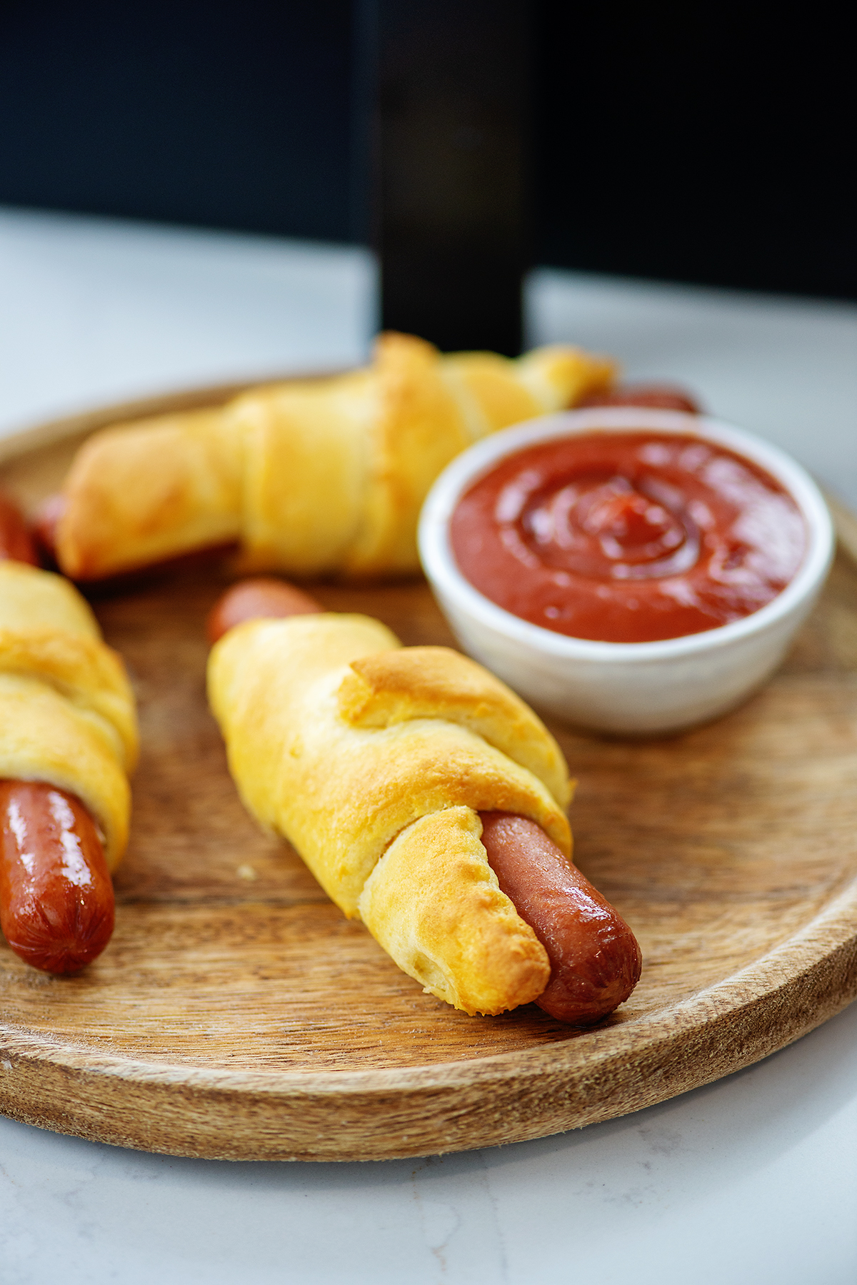 pigs in a blanket on wooden cutting board with ketchup.