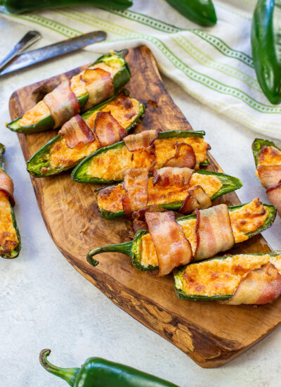 Jalapeno poppers on a cutting board surrounded by jalapeno peppers.