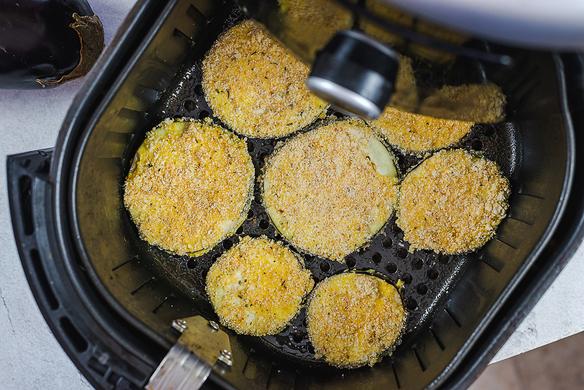 Overhead view of breaded egg plant in an air fryer basket.