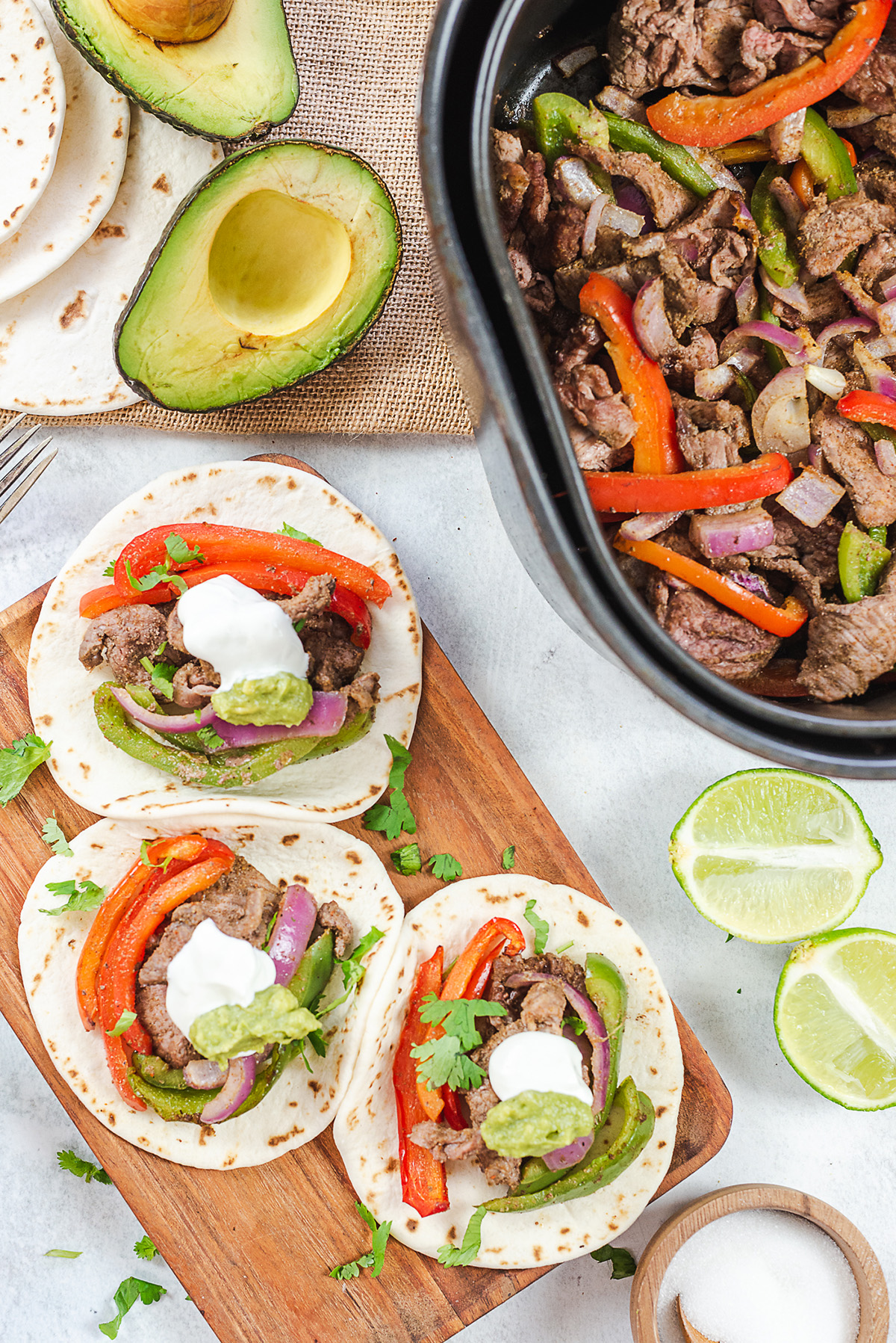 Steak fajitas and avocados in front of an air fryer basket.