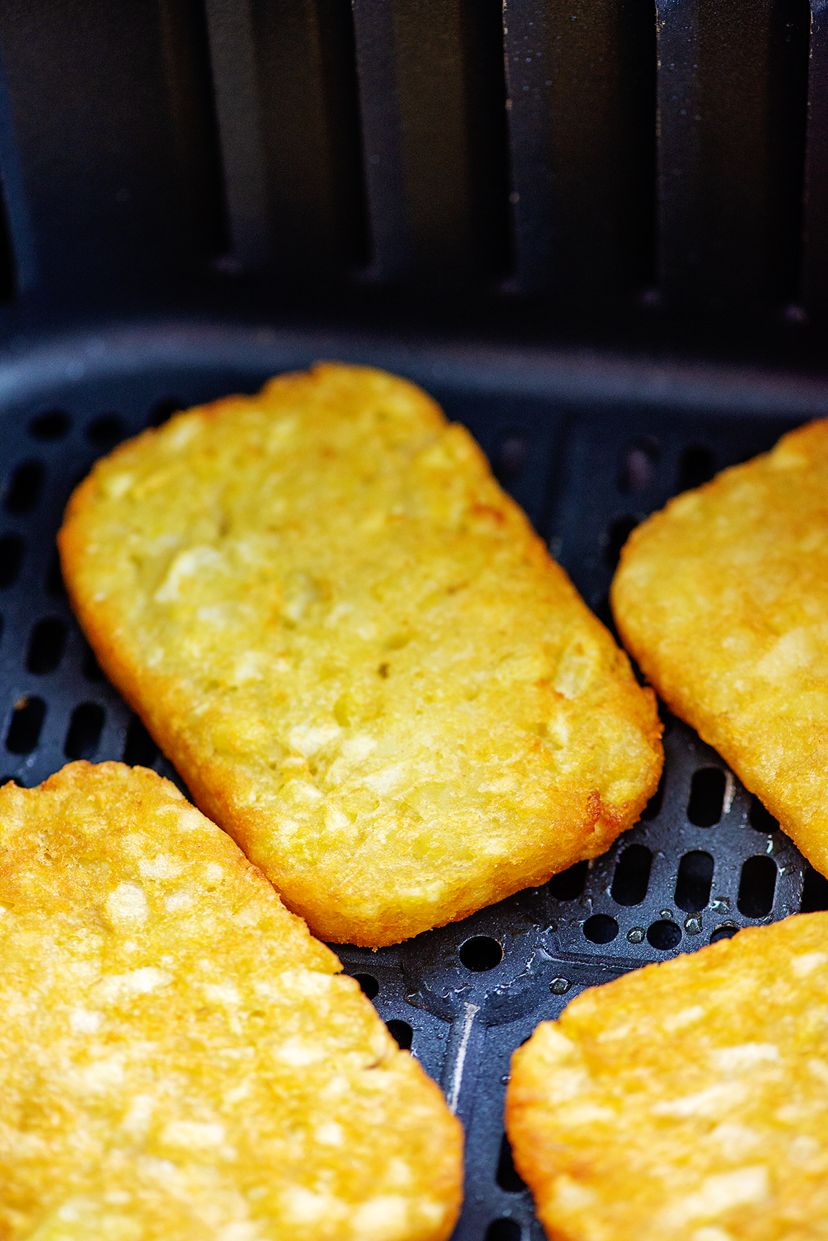 A few cooked hashbrowns in an air fryer basket.