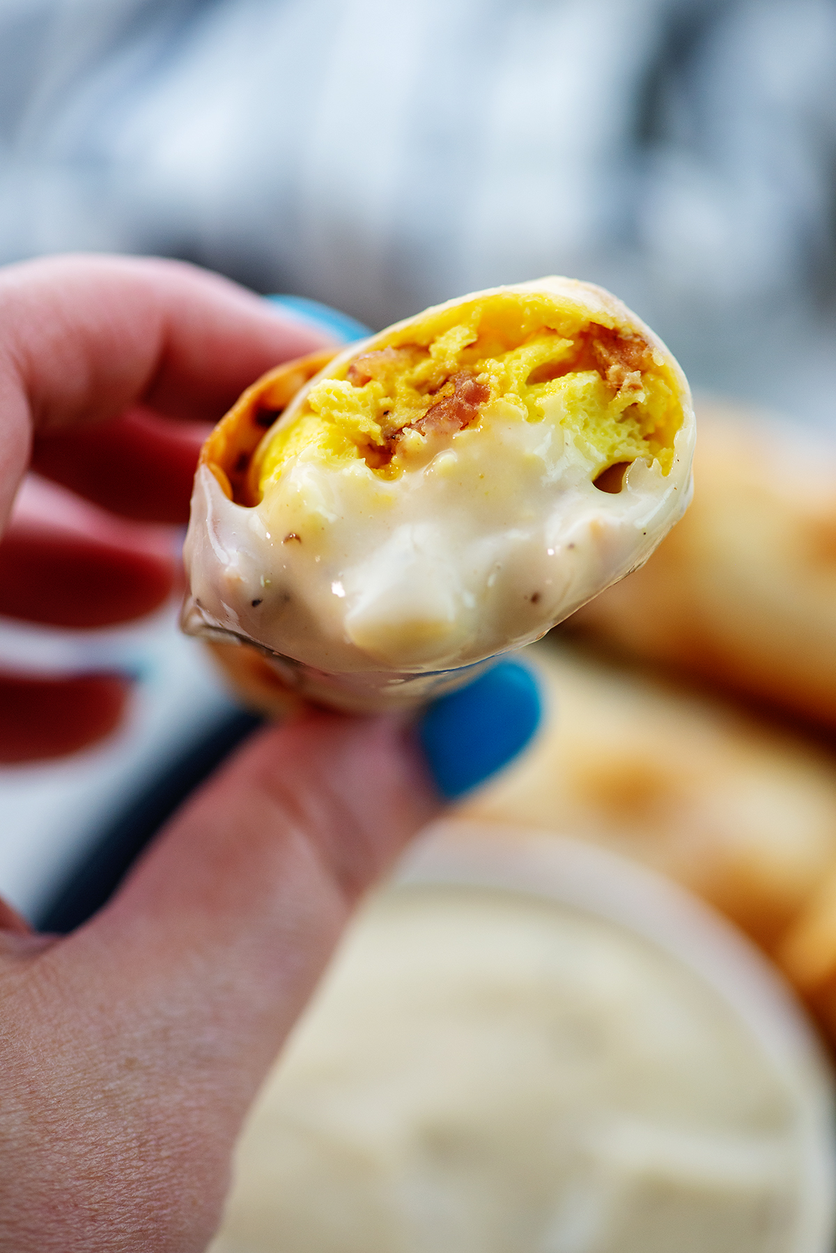 Close up of an egg roll dipped in gravy being held up to the camera.