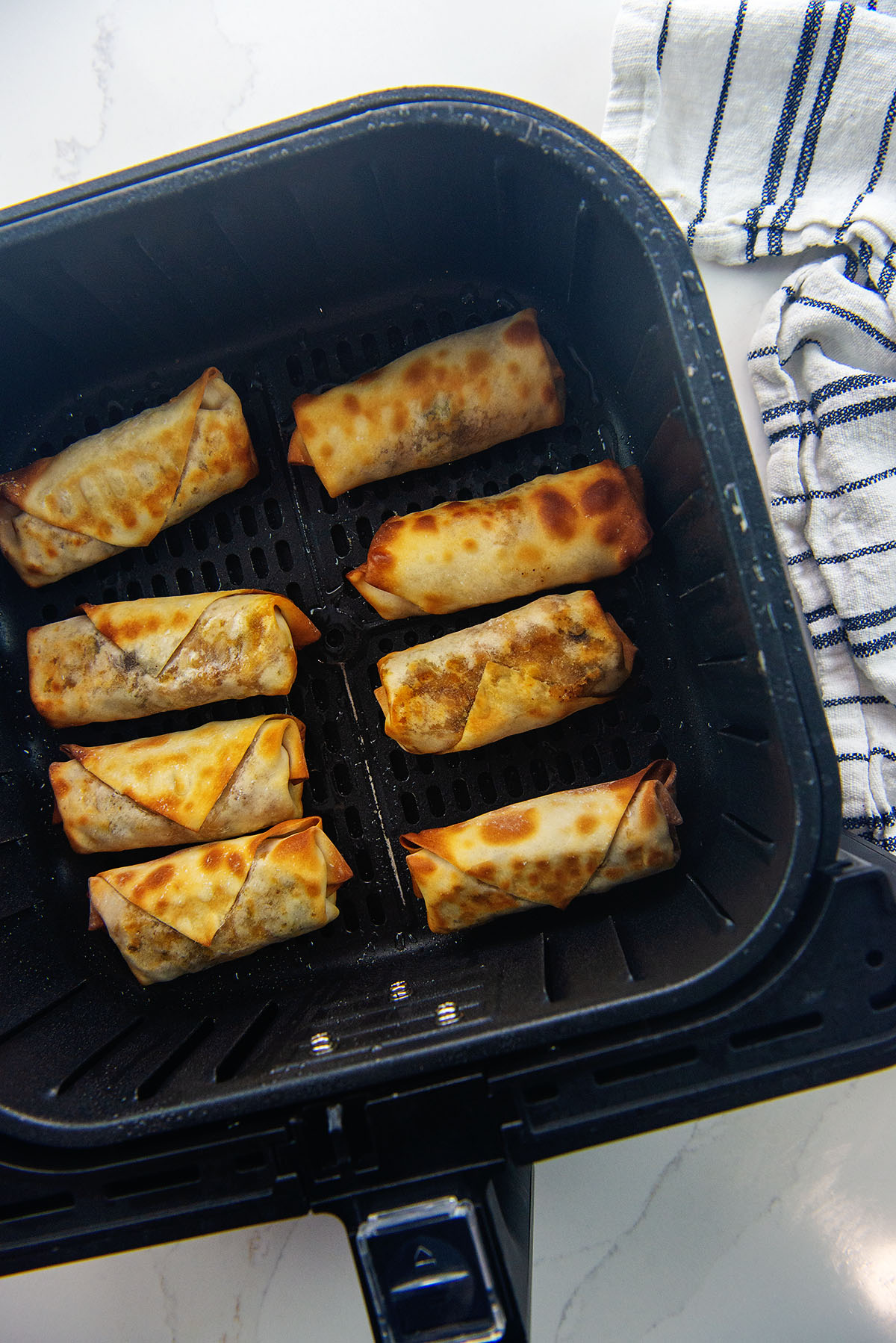 Overhead view of egg rolls spaced out in an air fryer basket.