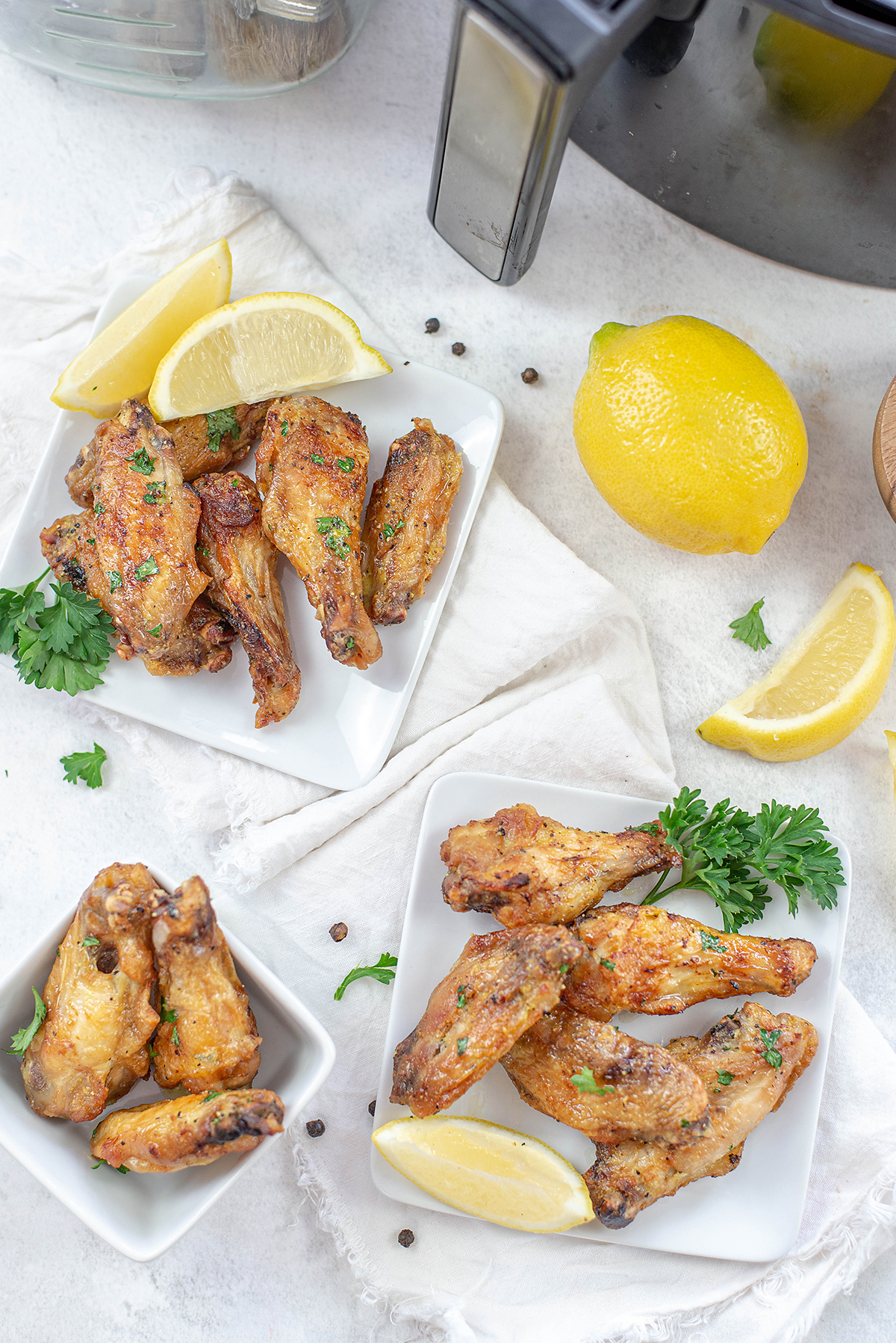 Two square plates of chicken wings in front of an air fryer.