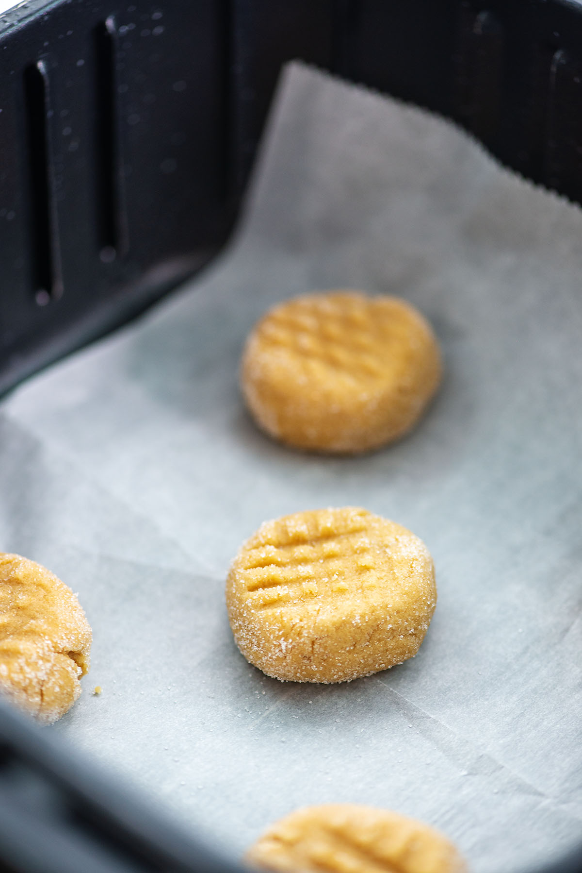Several raw peanut butter cookies in an air fryer basket.