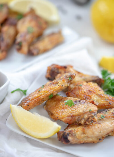 Close up of a lemon wedge and chicken wings on a square plate.