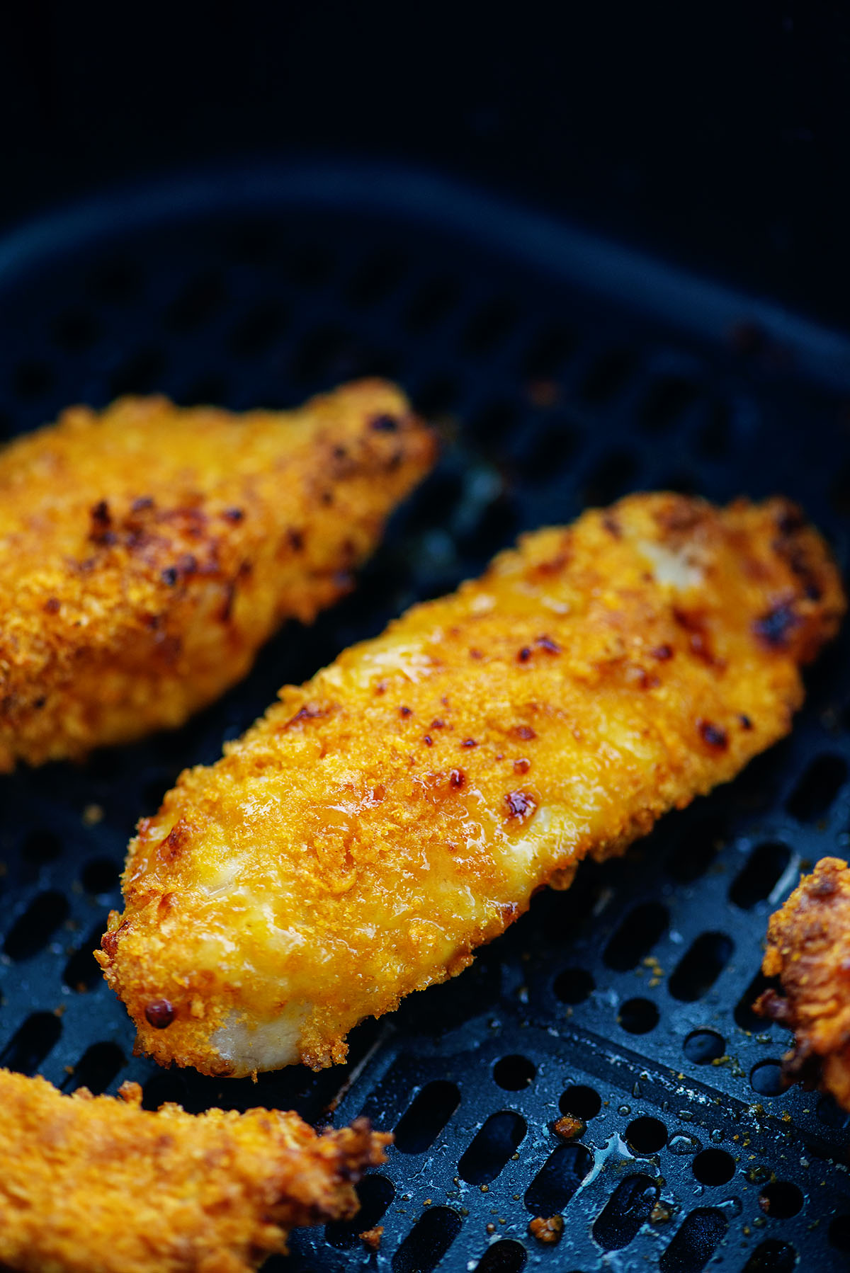 Close up of a chicken strip cooking in an air fryer basket.