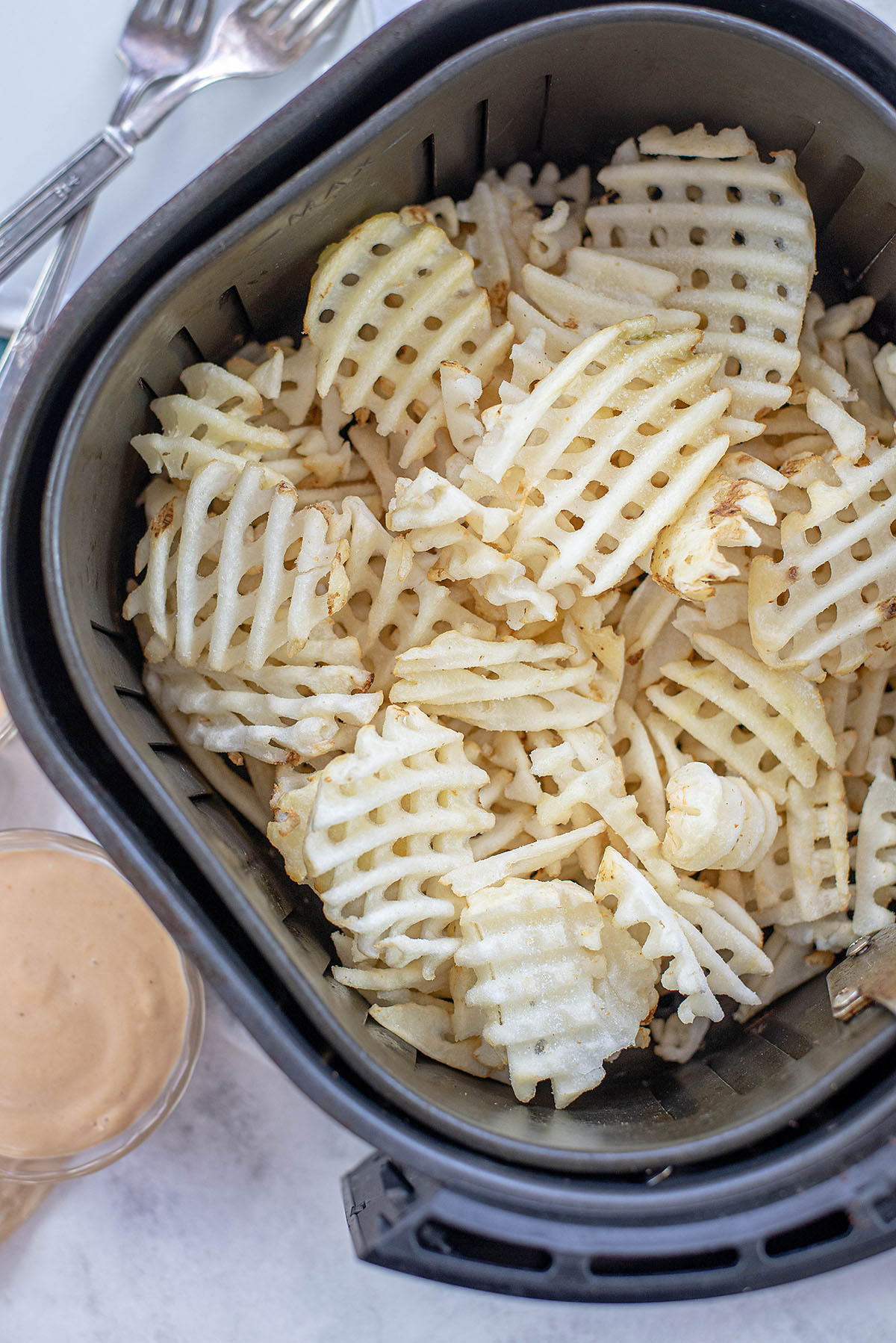 Frozen waffle fries piled in an air fryer basket.