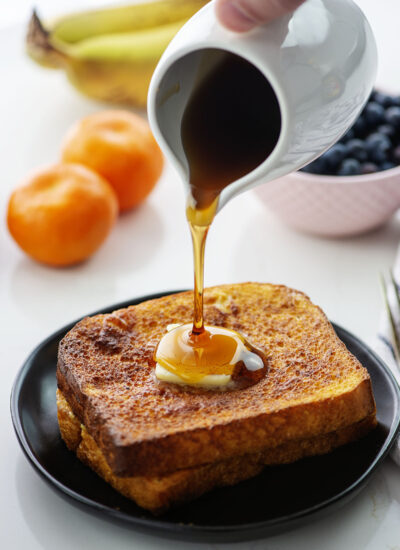 A person pouring syrup on two slices of French toast.