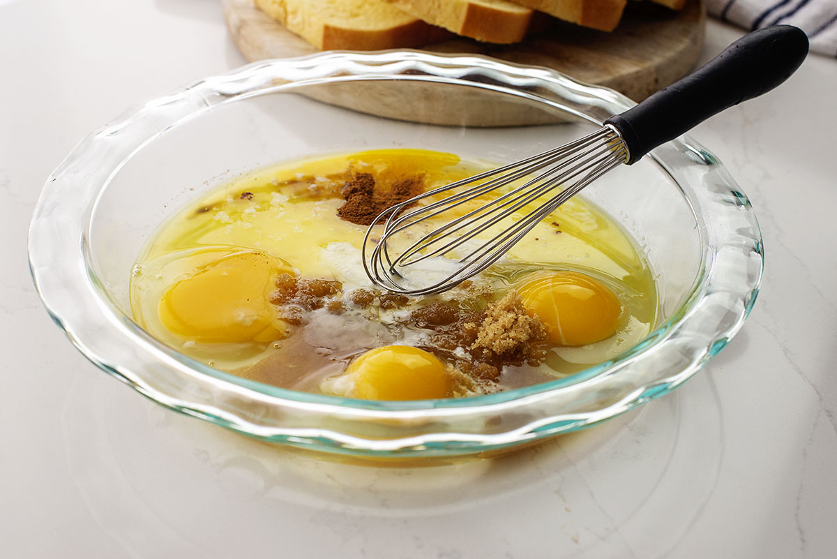 Eggs and brown sugar being whisked in a clear glass bowl.