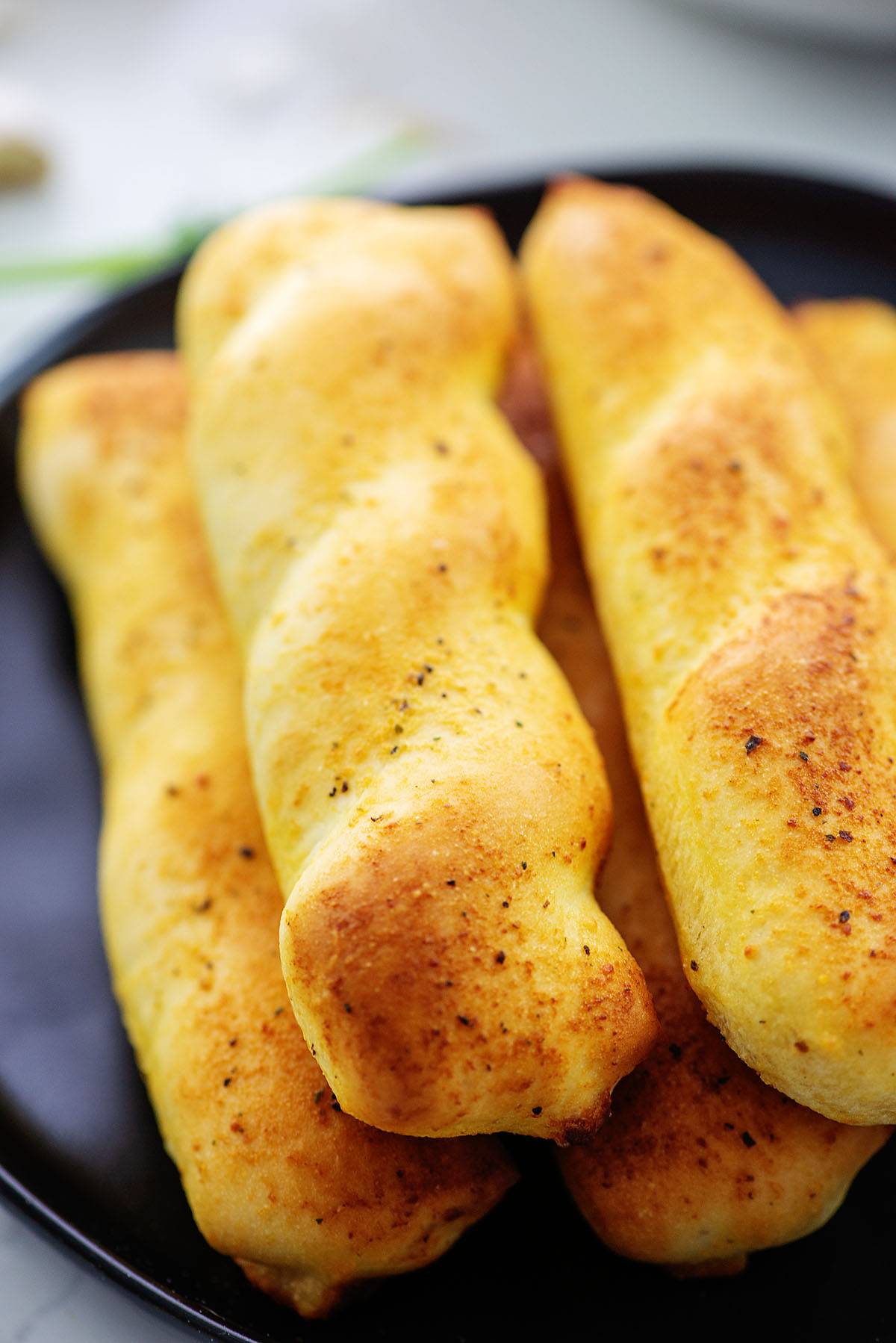 A pile of breadsticks on a small black plate.