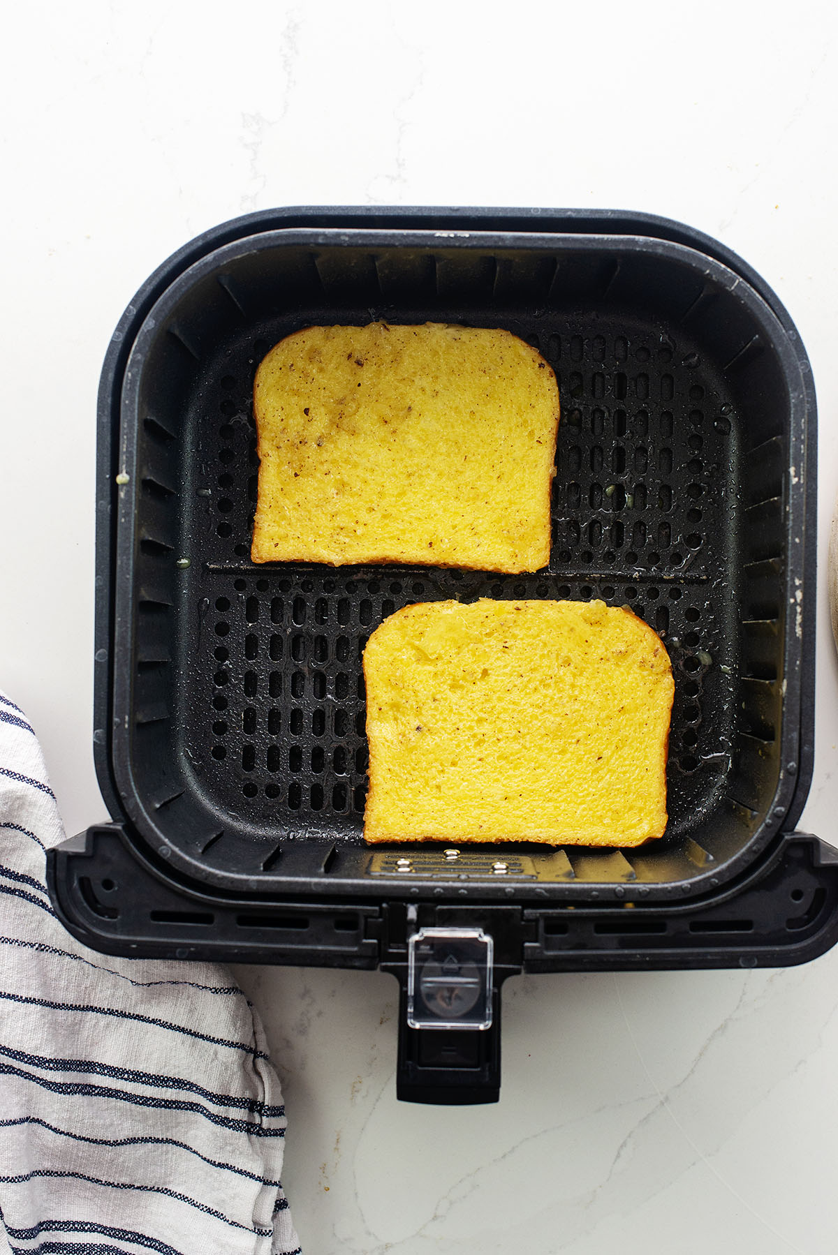 Two uncooked slices of French toast in an air fryer basket.