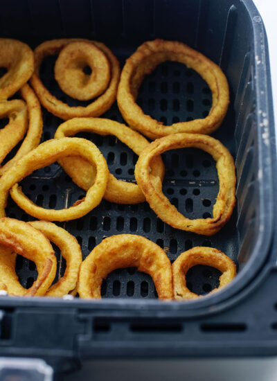 An air fryer basket with onion rings in it.