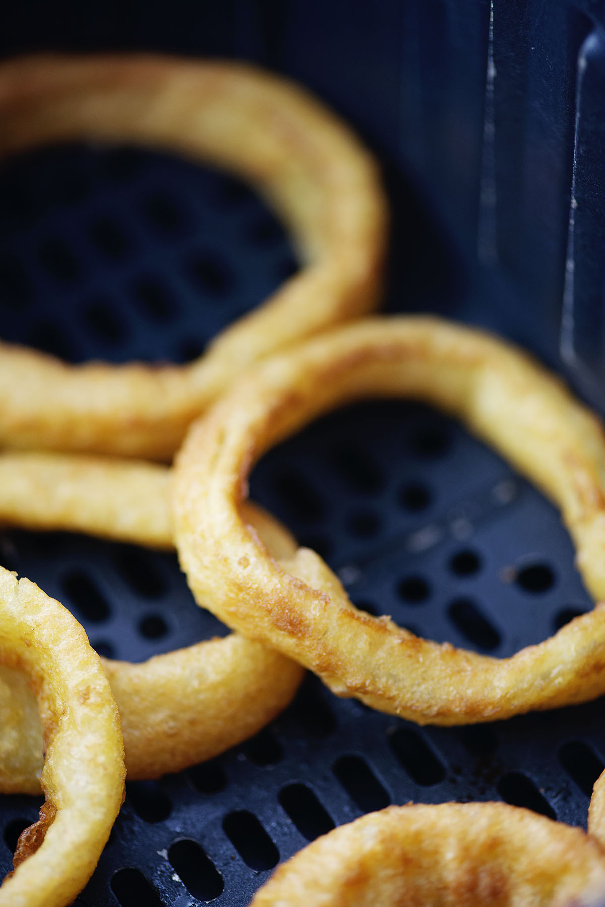 Close up of an onion ring in an air fryer basket.