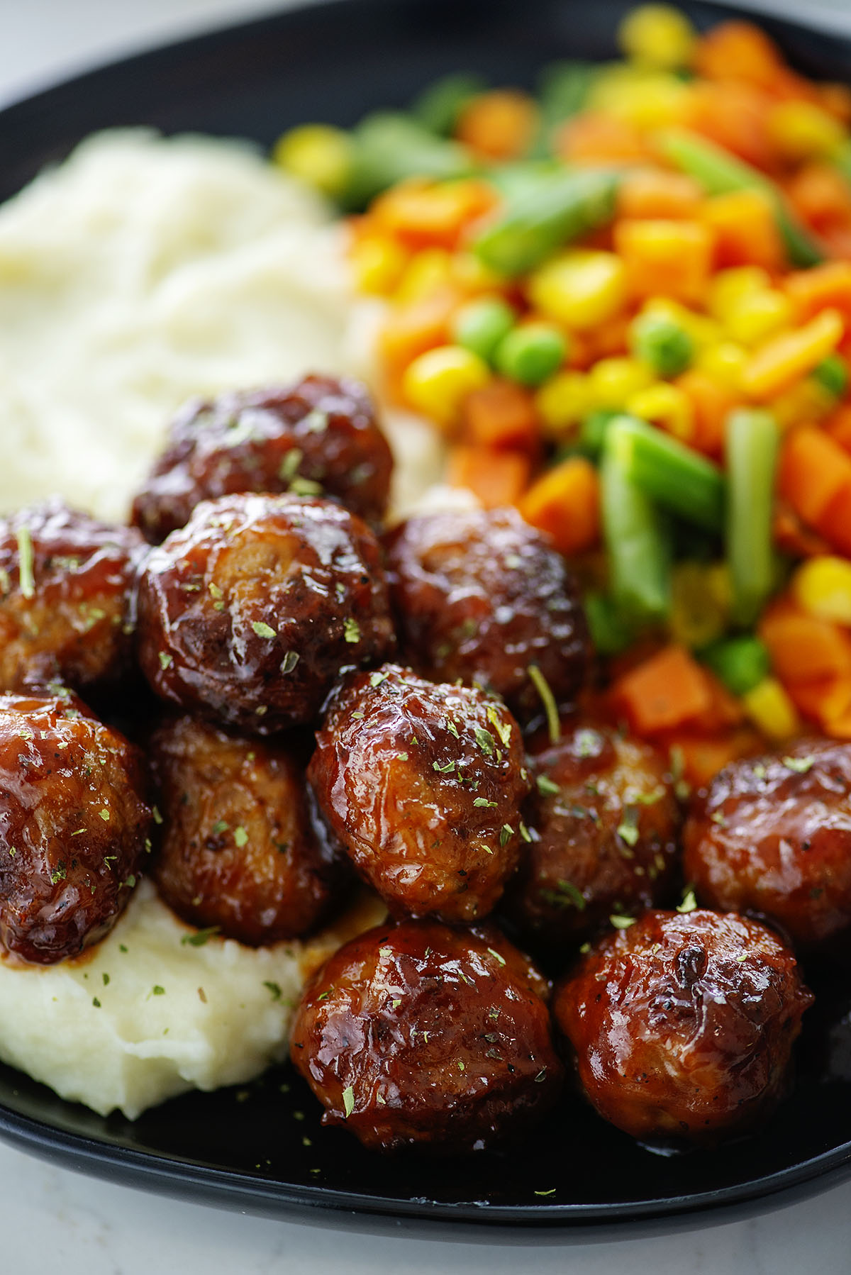 BBQ meatballs on plate with potatoes and vegetables.