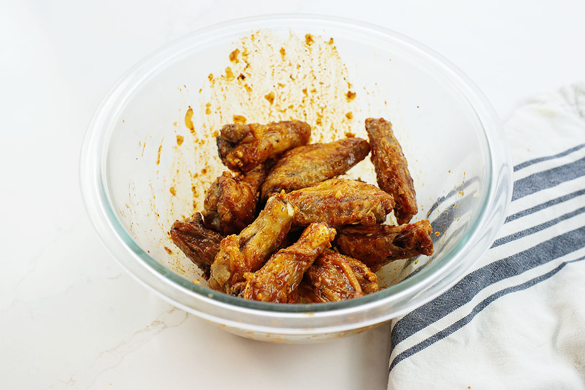 Cooked chicken wings in a clear glass bowl with seasoning.