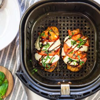 Air fryer basket on a countertop with chicken caprese in it.