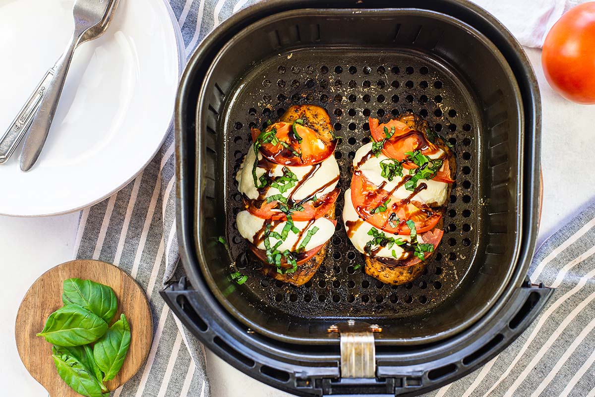 Air fryer basket on a countertop with chicken caprese in it.