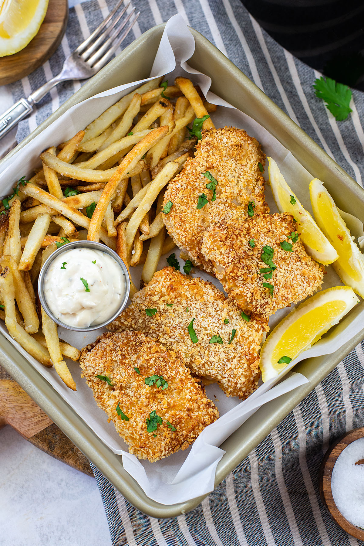 A square plate with fries, fish, and lemon wedges on it.