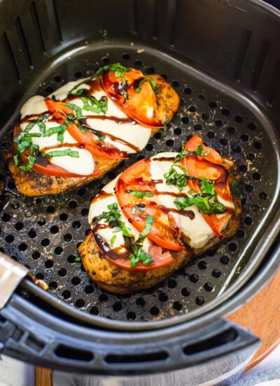 Two cooked chicken caprese in an air fryer basket.