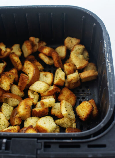 Croutons piled up in an air fryer basket.
