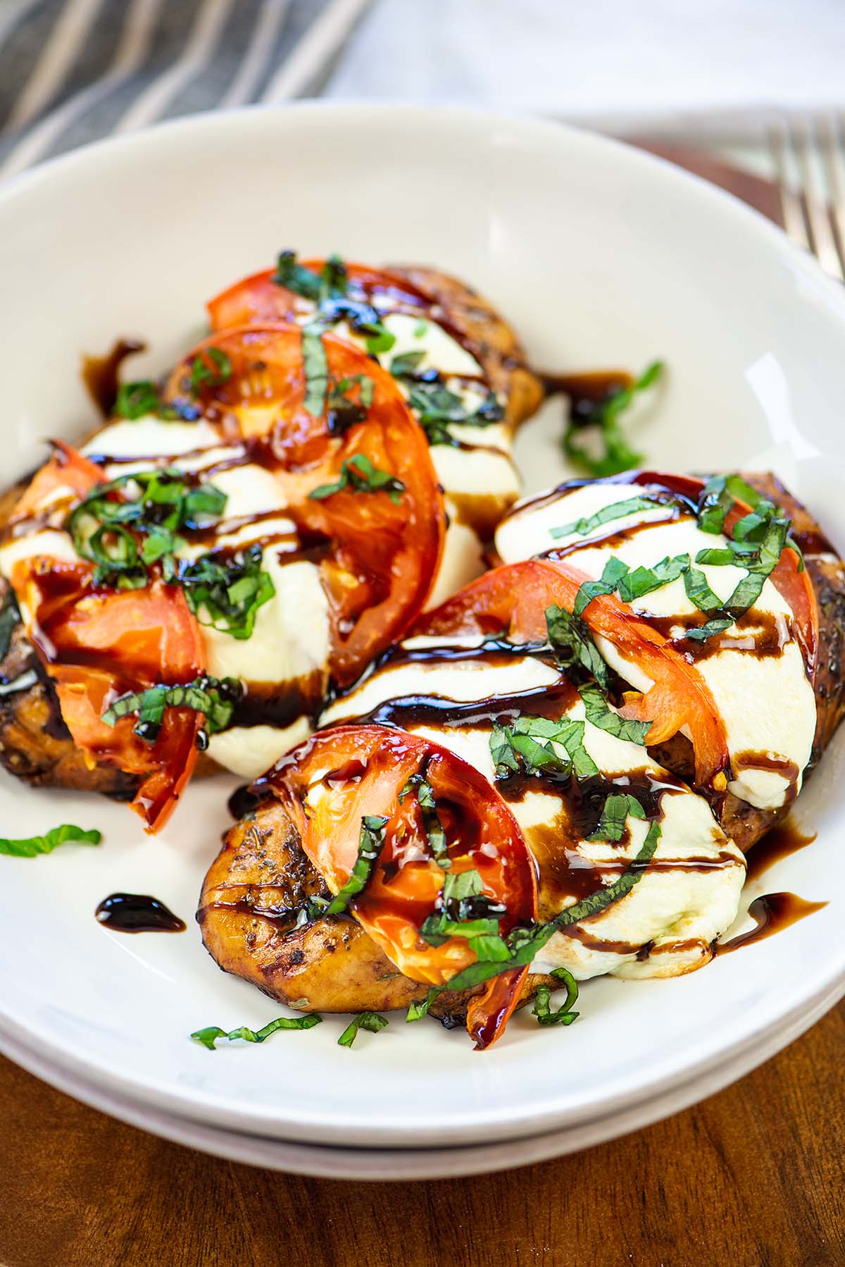 Two chicken caprese on a white round plate.