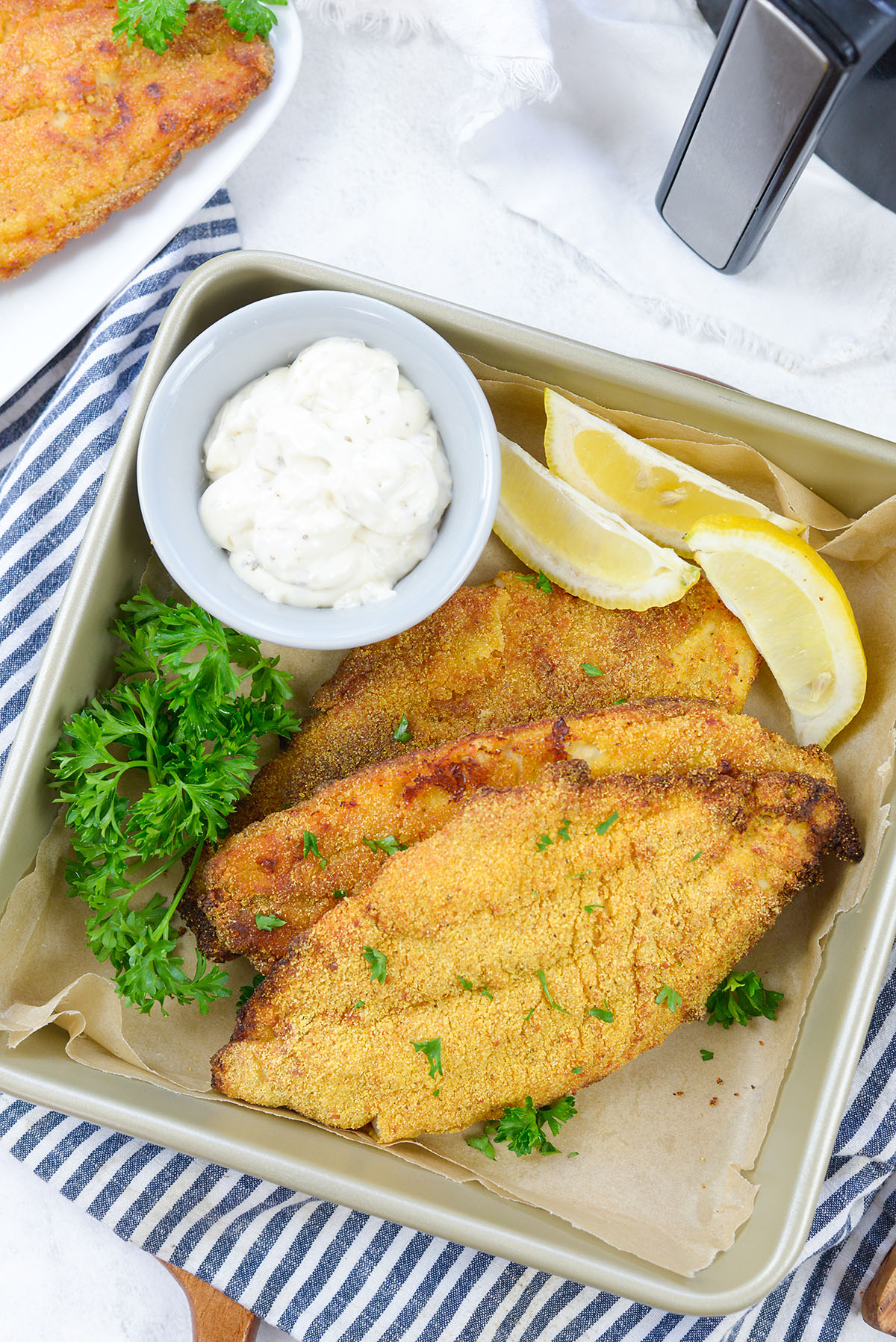 Overhead view of a tray of catfish fillets with lemon wedges.