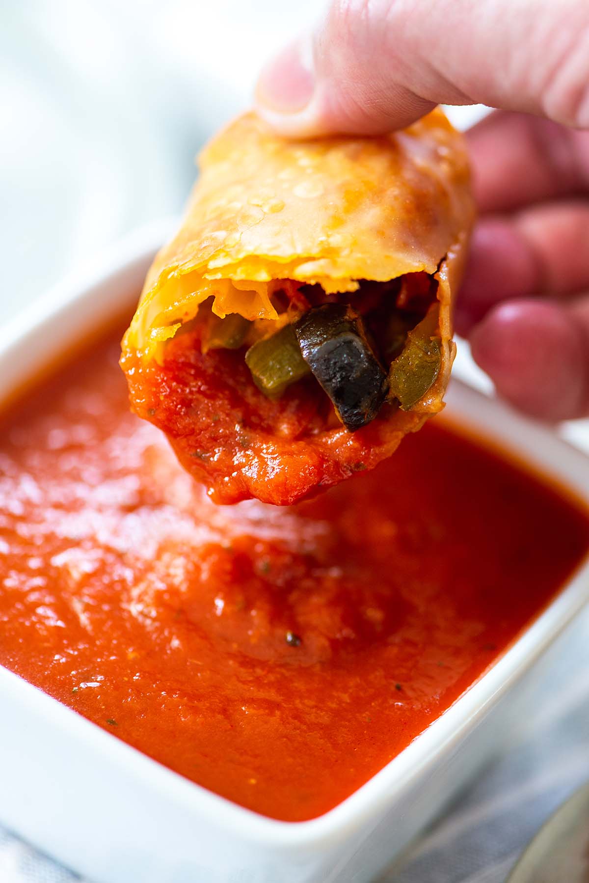 Person dipping an egg roll into pizza sauce.