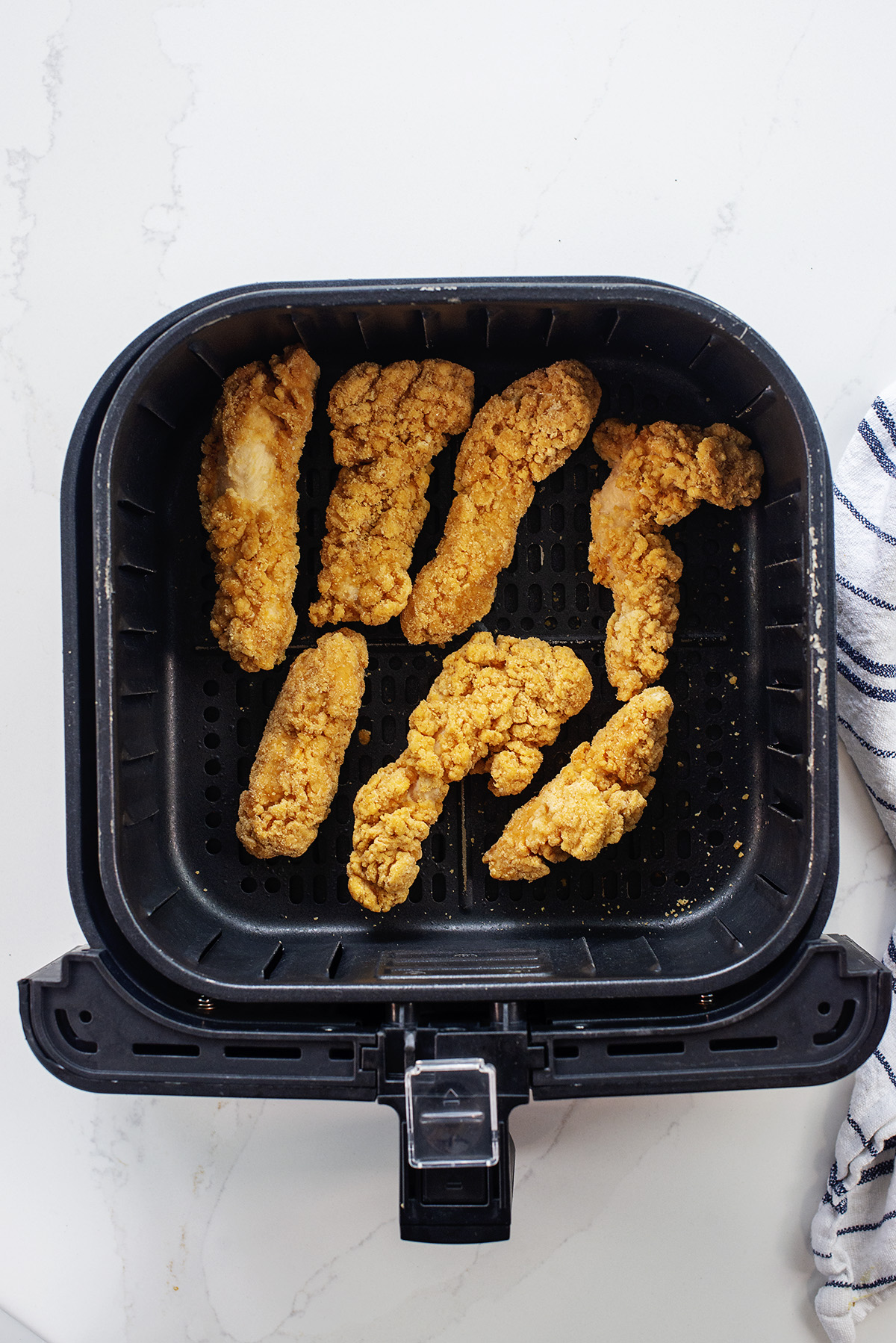 Seven chicken strips in an air fryer basket.
