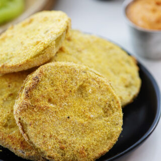 Stacked fried green tomatoes on a small black plate.
