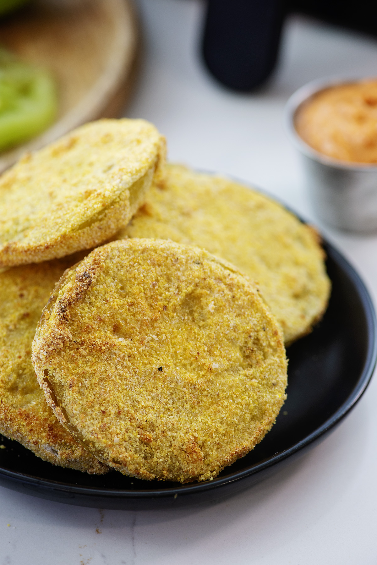 Stacked fried green tomatoes on a small black plate.