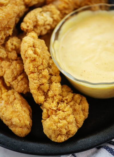 Close up of chicken strips and honey mustard sauce on a small black plate.