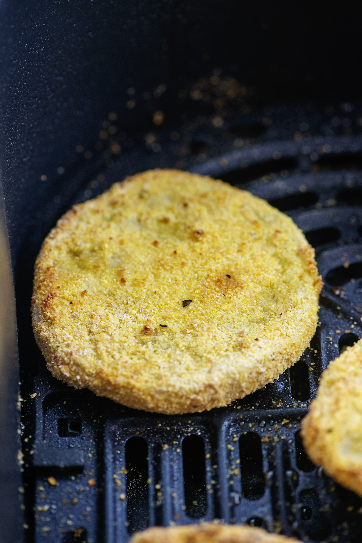 Close up of a slice of a fried green tomato in an air fryer.
