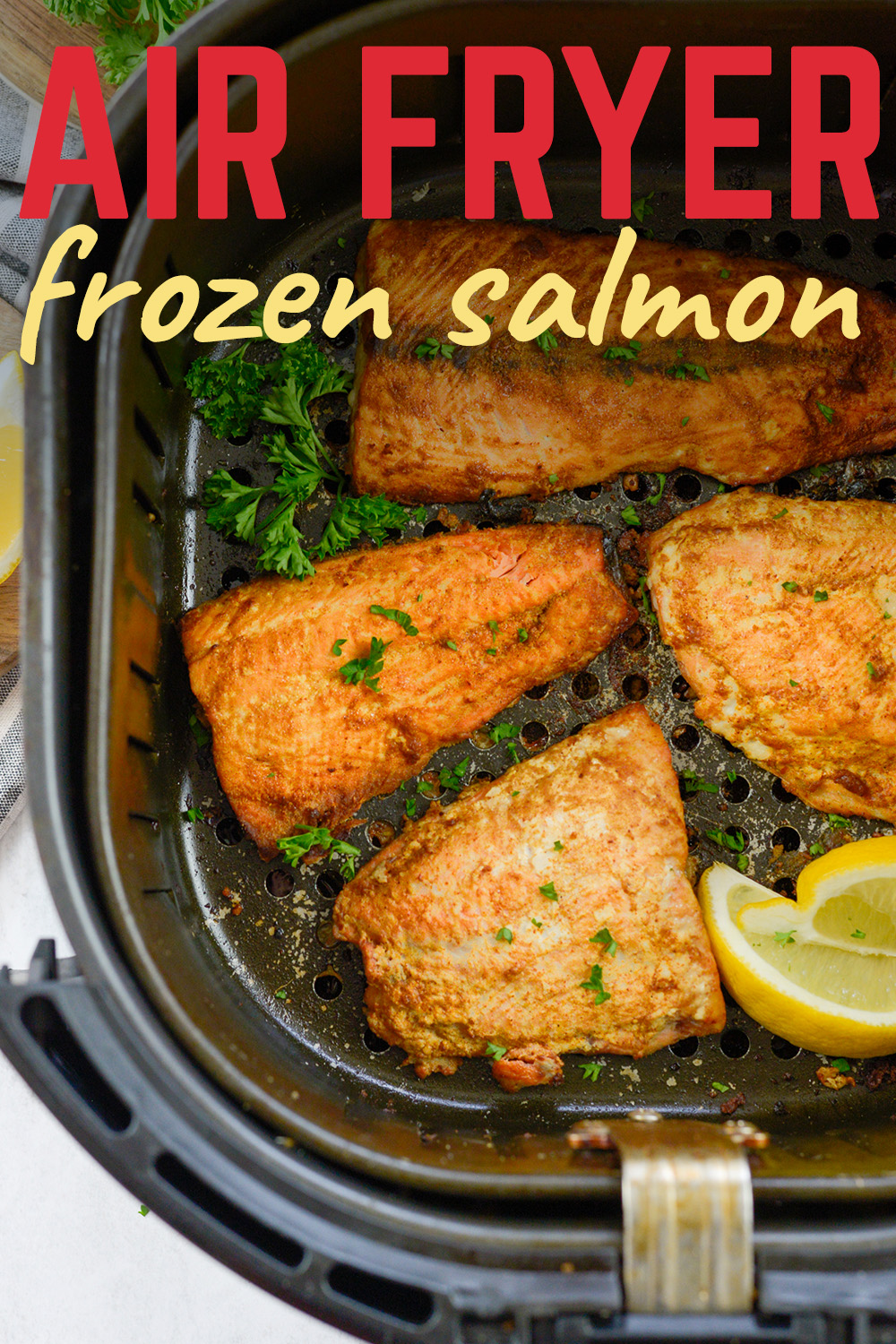 Four salmon fillets and a couple lemon wedges in an air fryer.