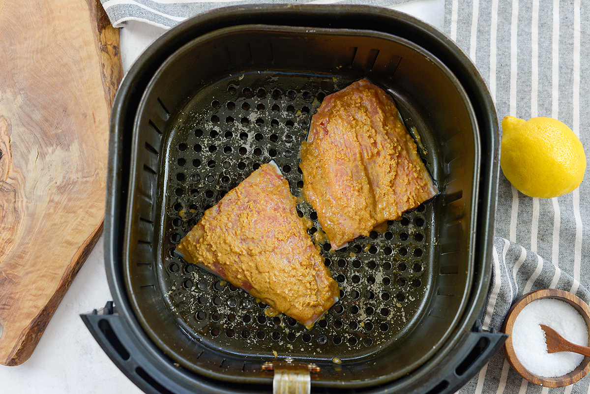 Seasoned raw salmon in an air fryer basket.