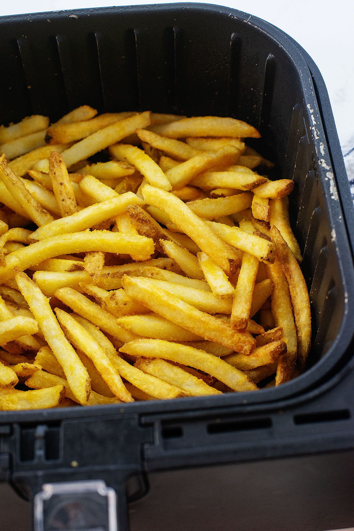 Cooked French fries in an air fryer basket.