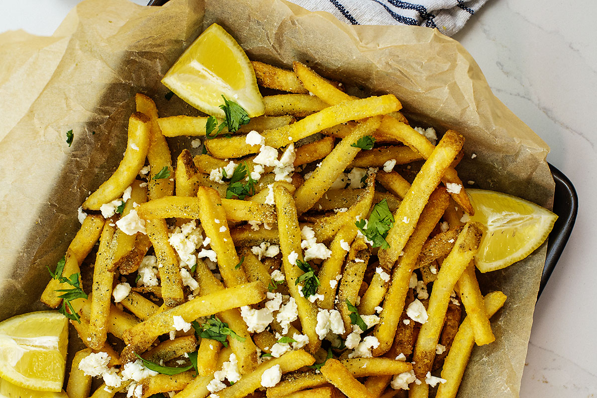 French fries with feta cheese and seasoning on them on a paper lined sheet pan.