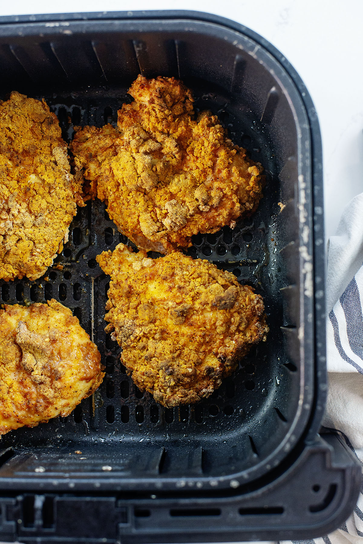 Four chicken breasts in an air fryer basket.
