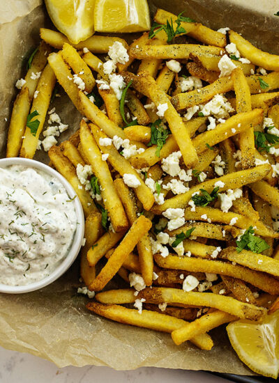 Overhead view of French fries with feta cheese and seasoning on them with a cup of tatziki sauce.